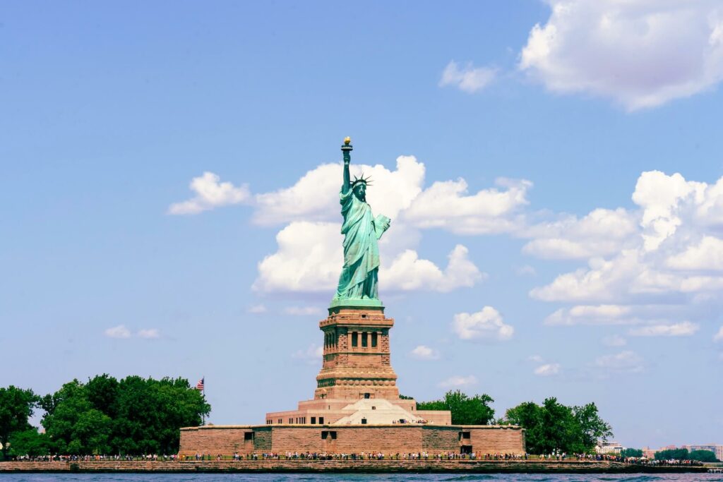 The statue of liberty appears against a blue sky with clouds